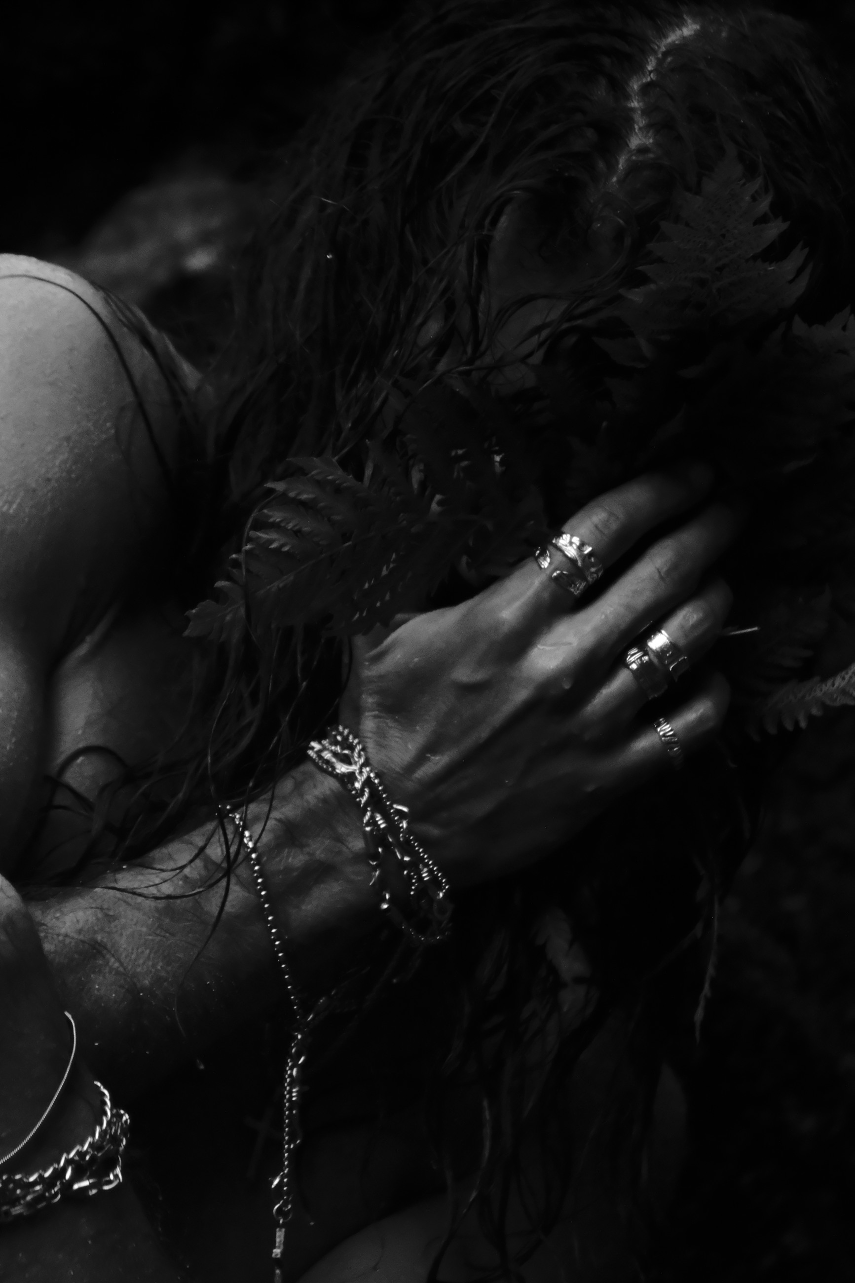 Monochrome portrait behind ferns, hands adorned with silver rings