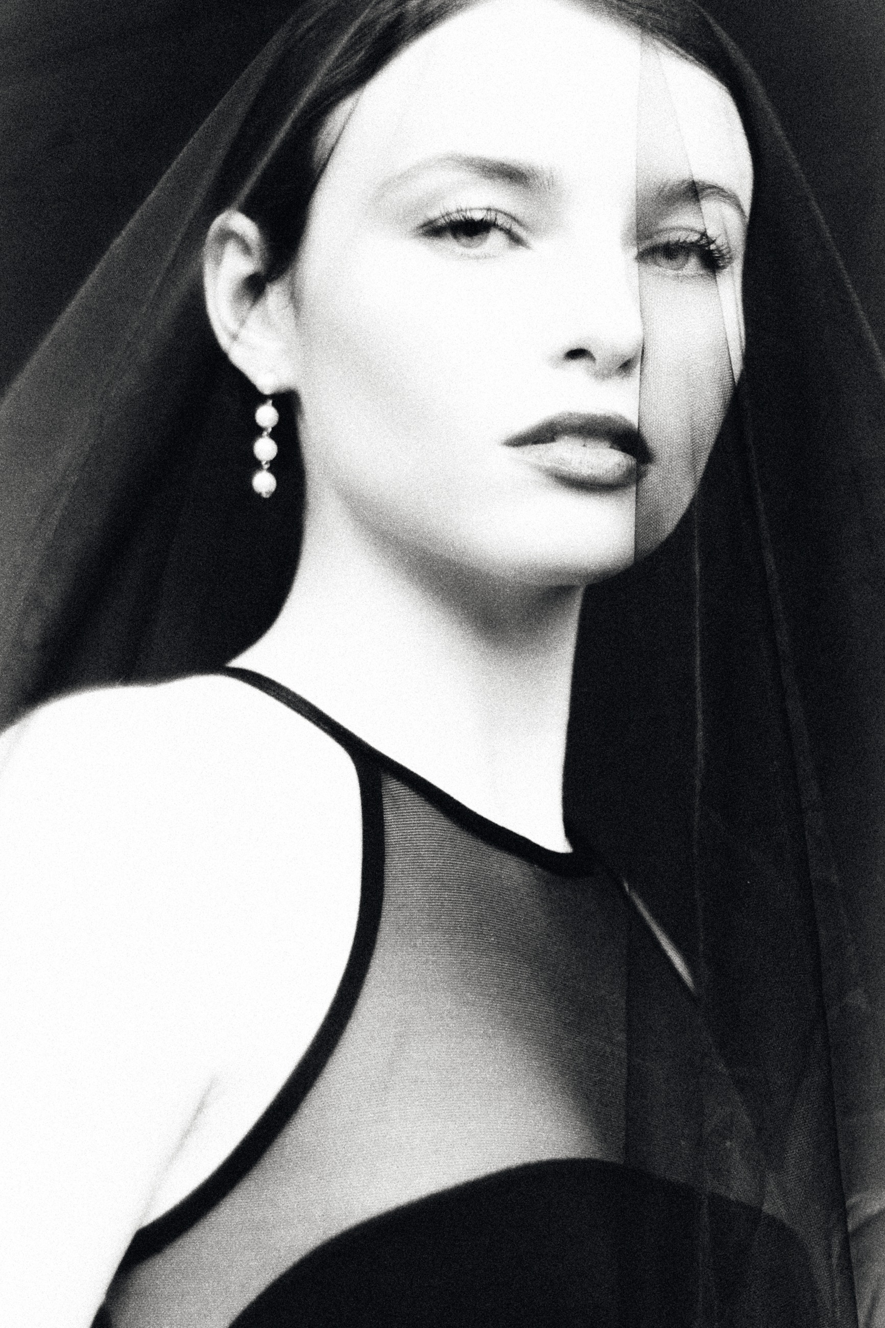 Close portrait with a sheer black veil and pearl earrings