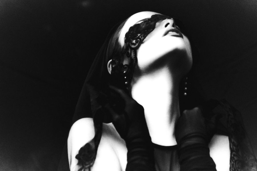 Black and white portrait of a woman in a dark lace veil, eyes closed, face turned up toward the light